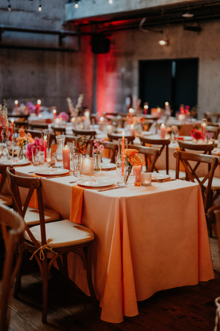 Long reception tables dressed in orange linen in an event hall, Emett Joseph Photography
