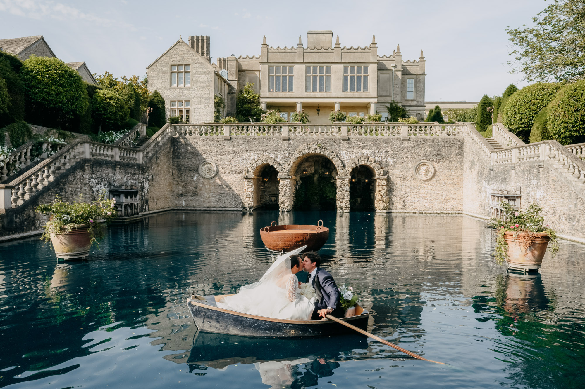 A couple in a rowing boat on the stone-walled pool below the house at Euridge Manor, on the edge of the Cotswolds, Emma-Jane Photography