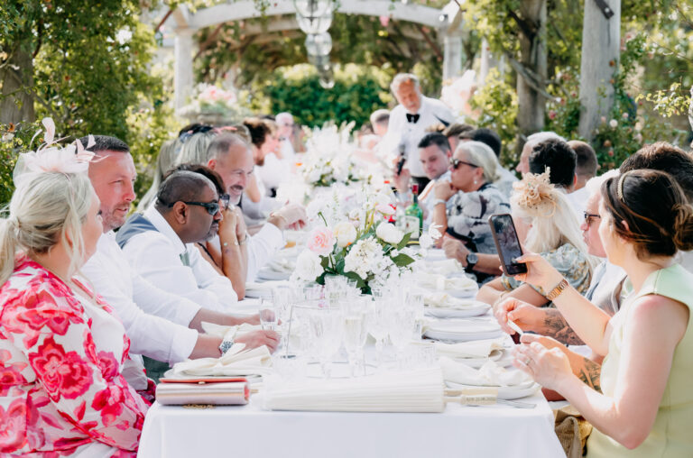 Guests at a long table for dinner under the pergola in the rose garden at Euridge Manor, Emma-Jane Photography
