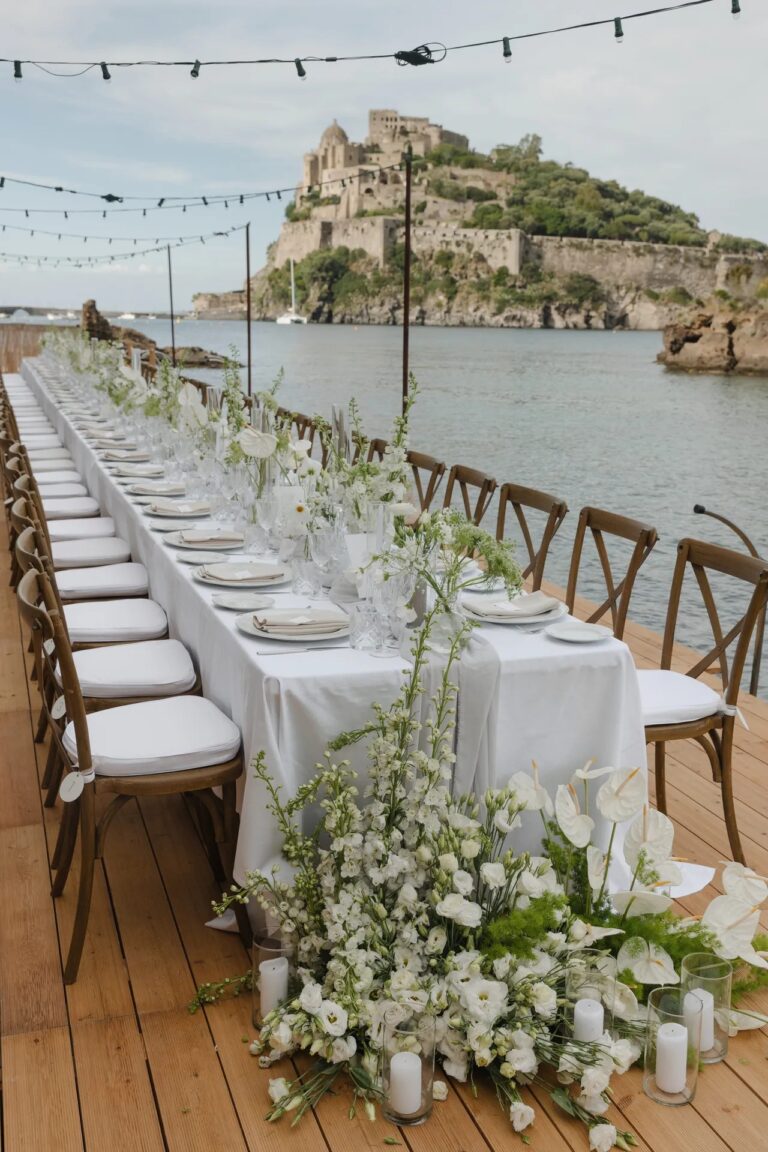 A long table on a wooden deck at the water, the castle beyond, Ester Chianelli Weddings & Events