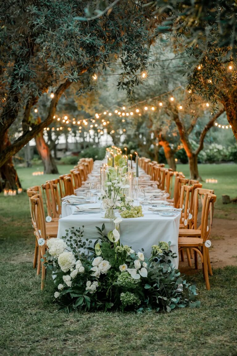 A long table under the olives, festoon lights strung above it, Ester Chianelli Weddings & Events