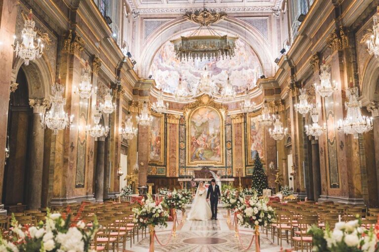 A ceremony in a gilded church with chandeliers, the aisle lined with white flowers, for the Tor Crescenza wedding, Eventilab Weddings