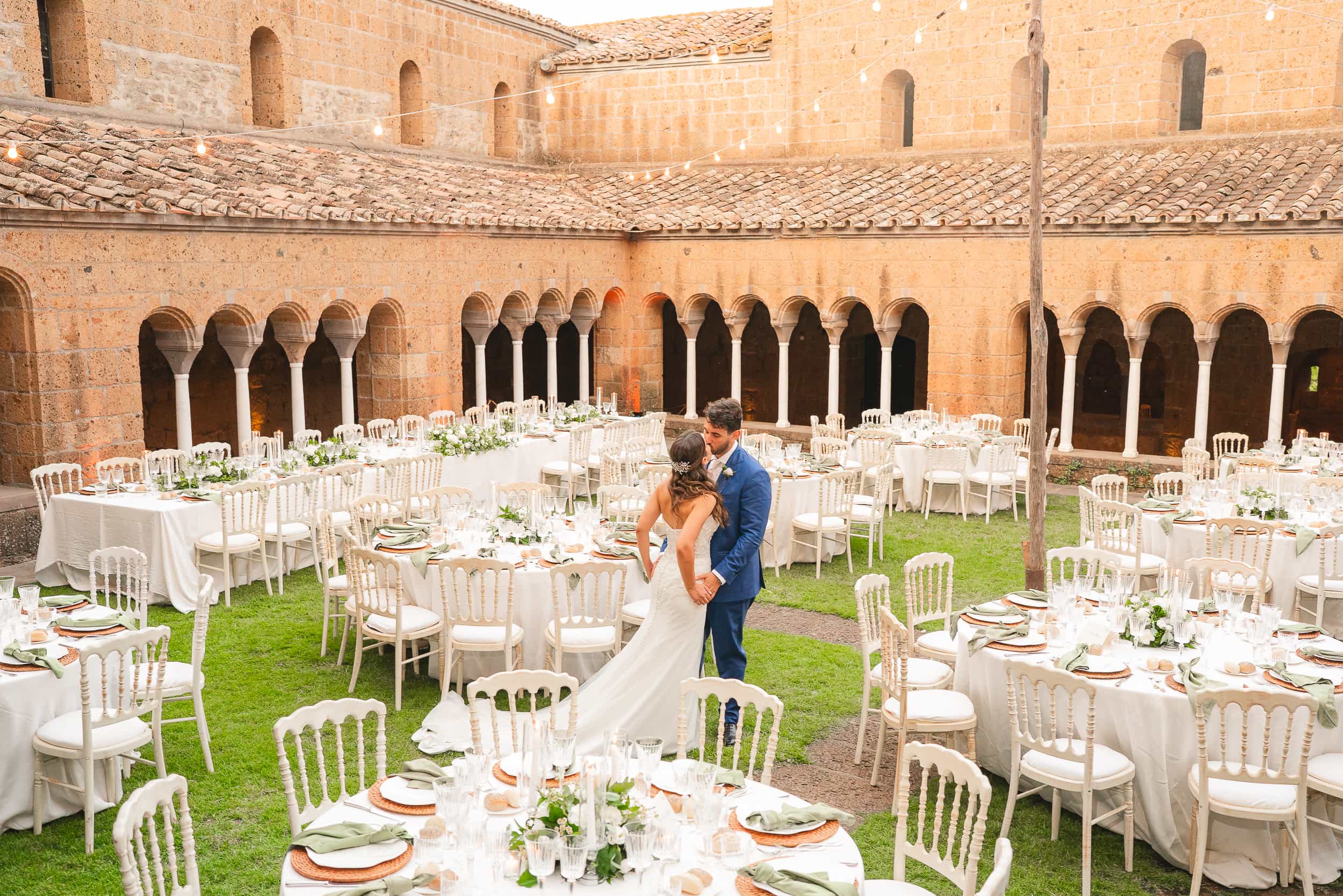 Dinner tables laid on the lawn of the cloister at the Abbazia di San Giusto, the couple among them, Eventilab Weddings