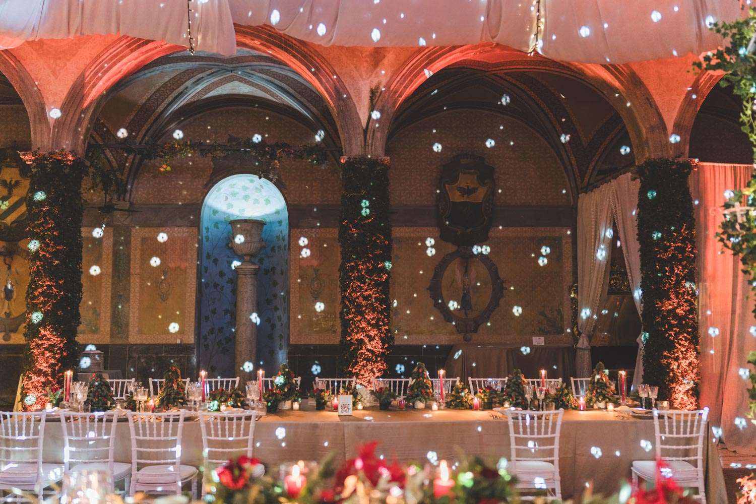 Reception at Castello di Tor Crescenza, a long table under arches dressed with greenery and projected light, Eventilab Weddings