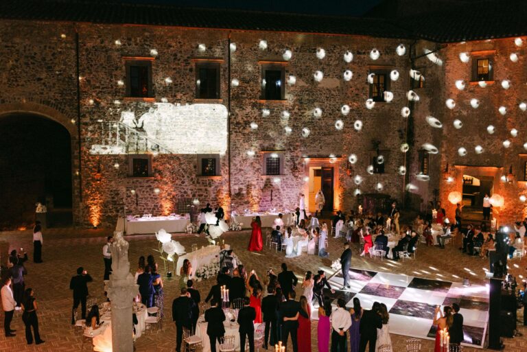 Evening party in the courtyard of the Castello di Bracciano, lights projected across the stone walls, Eventilab Weddings