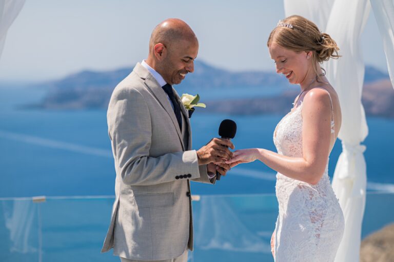 A couple exchange rings, the groom holding a microphone, with the sea behind them, Eventuries Wedding Planning and Styling