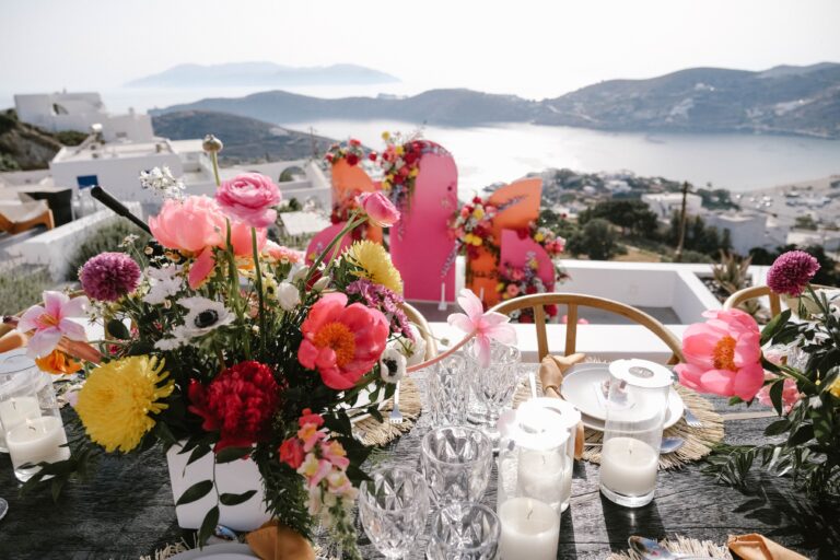 A colourful table arrangement of pink, red and yellow flowers overlooking the harbour in Ios, Eventuries Wedding Planning and Styling