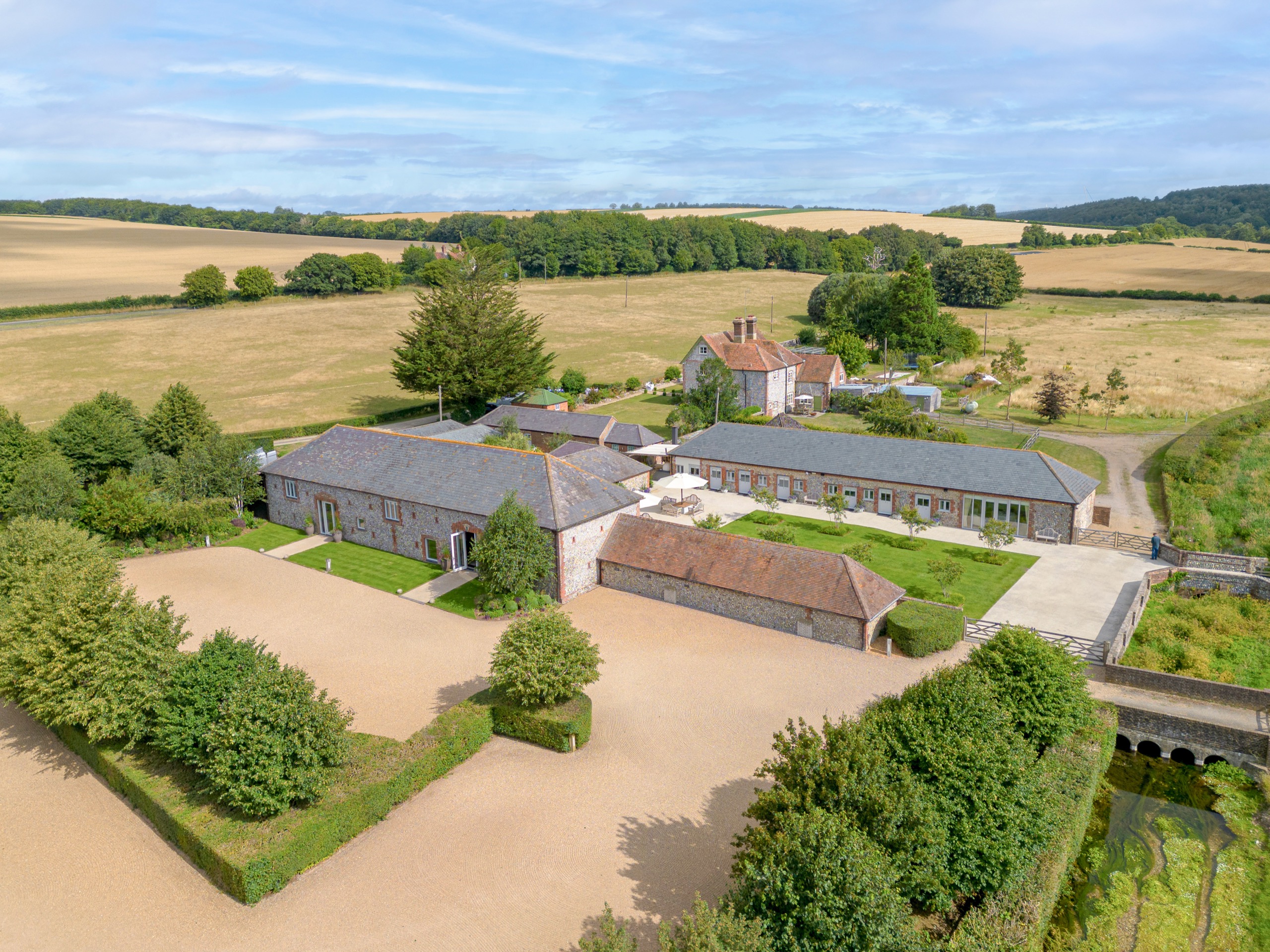 Farbridge from the air: the flint barns, courtyard and gravel turning circle in open farmland, with the South Downs behind, Farbridge