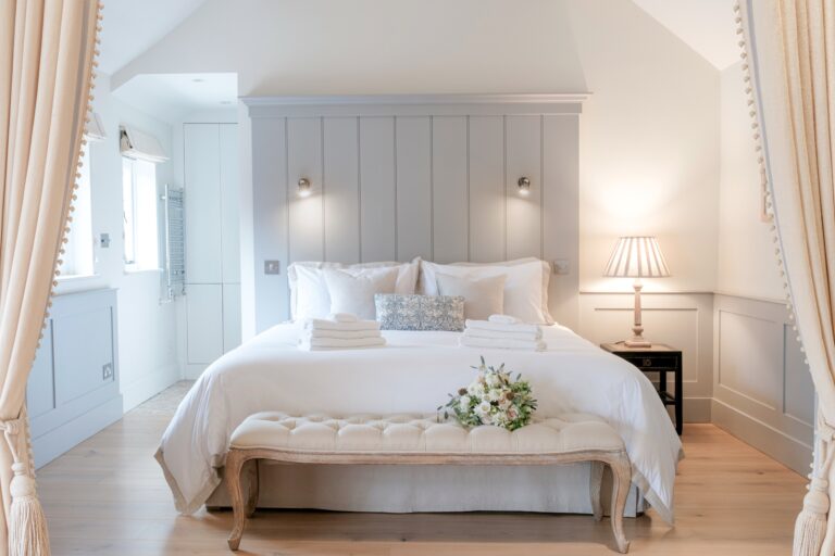 The bed in the couple's suite, with a panelled headboard, curtains and a bouquet on the footstool, Farbridge
