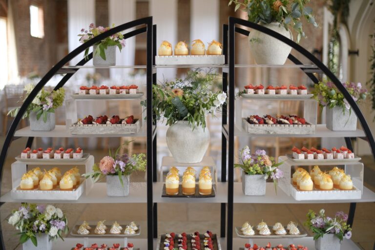 A dessert station of shelves stacked with small cakes, tarts and fresh flowers, Farbridge