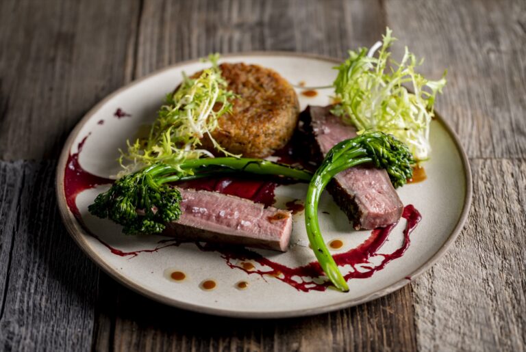 A plated main course of pink beef with tenderstem broccoli and a red wine reduction, Farbridge