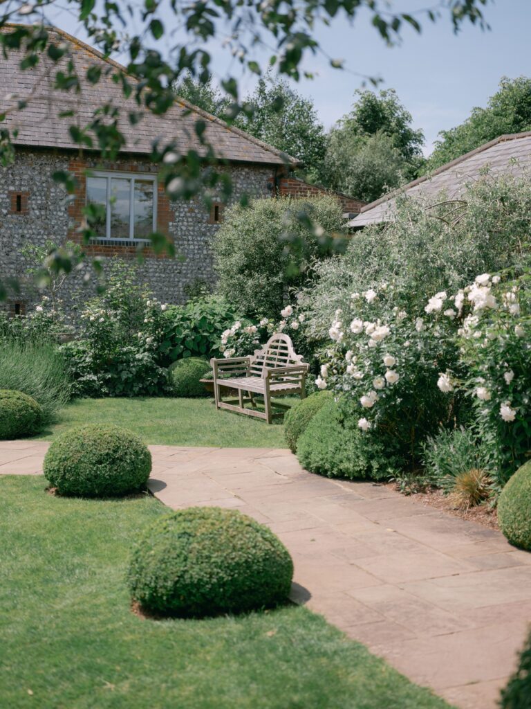 The private garden with clipped box, roses and a teak bench beside the flint buildings, Farbridge