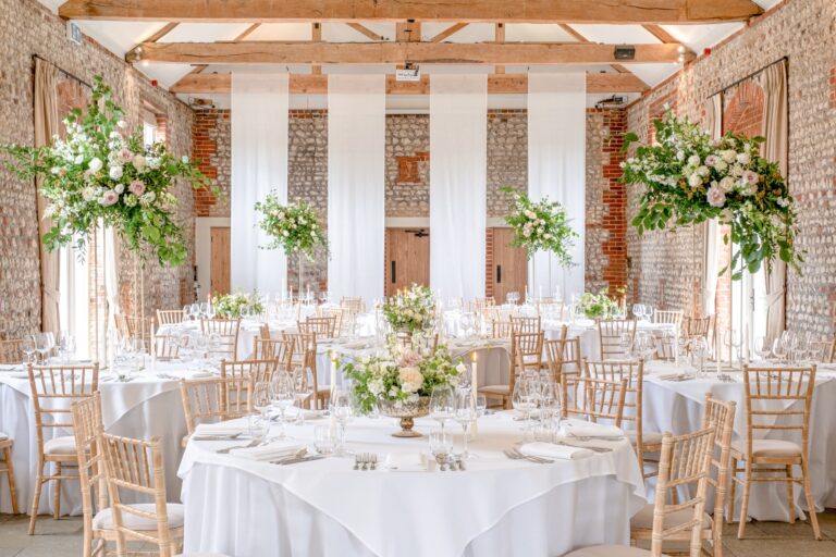 The Lavant Valley Barn set with round tables, white linen and tall floral arrangements under oak trusses, Farbridge