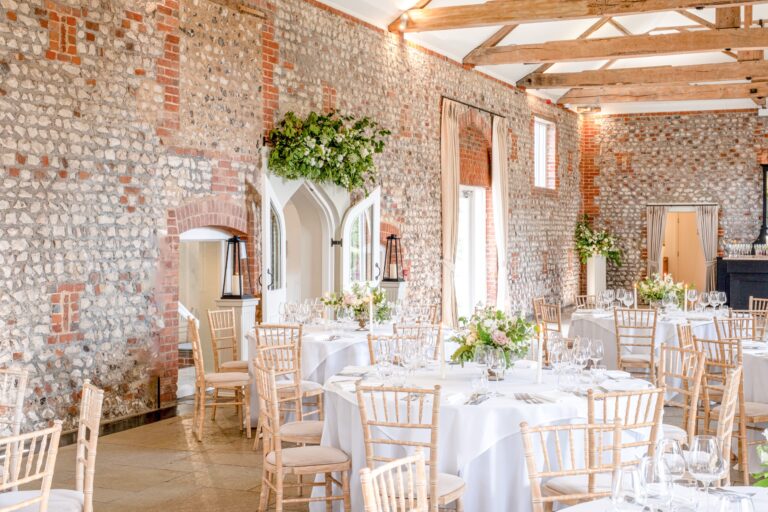 Flint and brick walls of the Lavant Valley Barn, with tables dressed in white and pale flowers, Farbridge