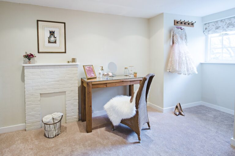 A dressing room in the Gatehouse with a mirror table and a wedding dress hung by the window, Farnham Castle