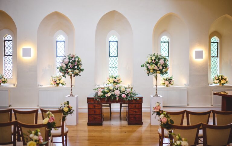 The registrar's table in the Lantern Hall, with flower stands in front of the tall leaded lancet windows, Farnham Castle