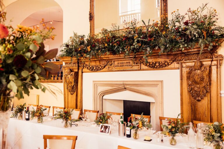 The top table in front of the carved wooden fireplace in the Great Hall, dressed with autumn foliage and flowers, Farnham Castle