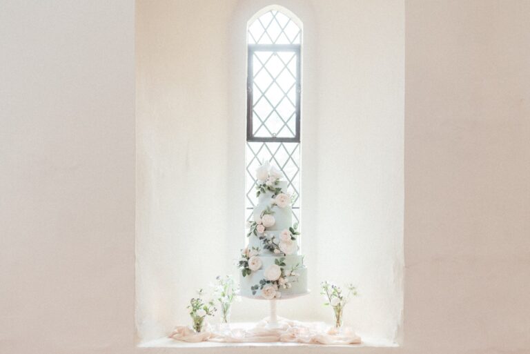 A tiered white wedding cake decorated with flowers, set in the deep recess of a lancet window, Farnham Castle
