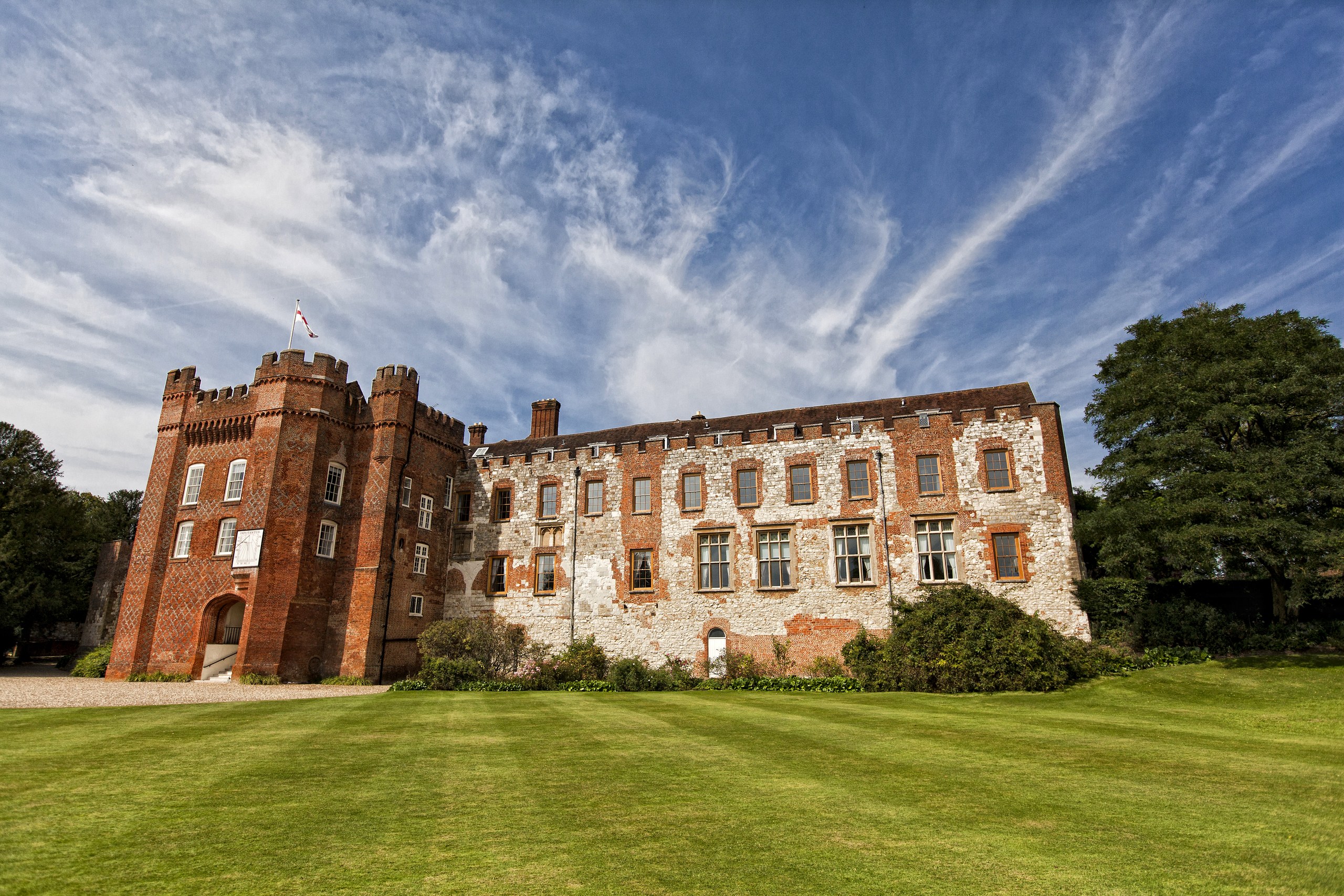 The brick entrance tower and flint-and-brick range of the Bishop's Palace seen across the striped Great Lawn, Farnham Castle