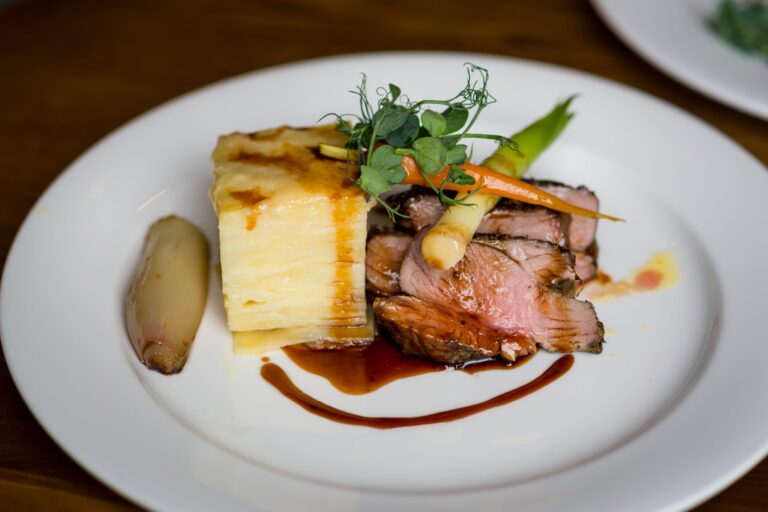 A plated main course of roast lamb with layered potato, glazed carrots and jus, Farnham Castle