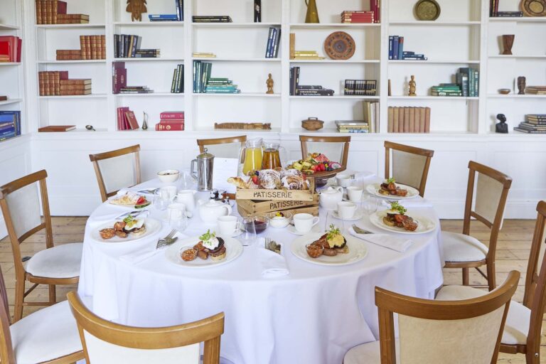 A round table laid for breakfast in front of white bookshelves, Farnham Castle