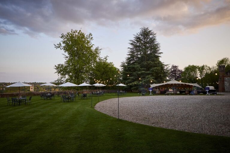 The Great Lawn at dusk, with parasols, festoon lights and the stretch canopy beside the gravel sweep, Farnham Castle