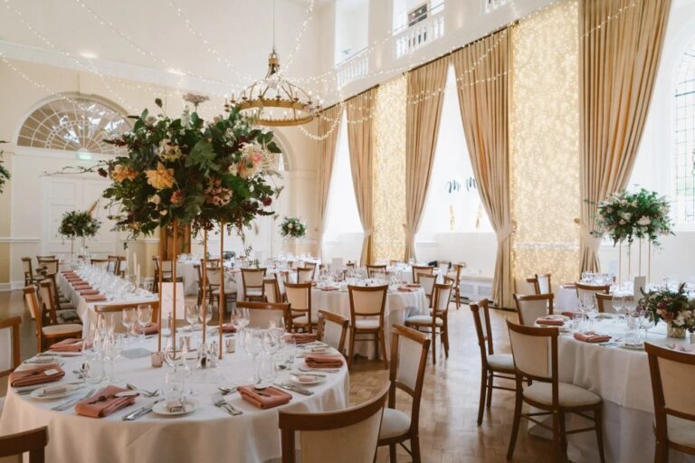 The Great Hall set with round tables and tall floral centrepieces, with curtains of fairy lights in the windows, Farnham Castle