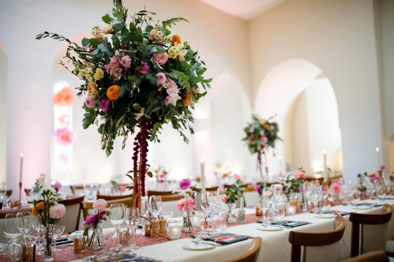 Long banquet tables in the Lantern Hall with tall arrangements of summer flowers and candles, Farnham Castle