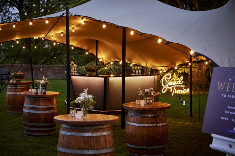 The festoon-lit canopy bar on the Great Lawn, with barrel tables and a neon sign, Farnham Castle