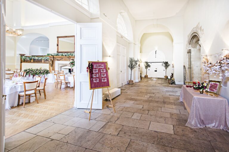 The flagstoned Stone Hall with a table plan on an easel and a view through to the Great Hall laid for dinner, Farnham Castle