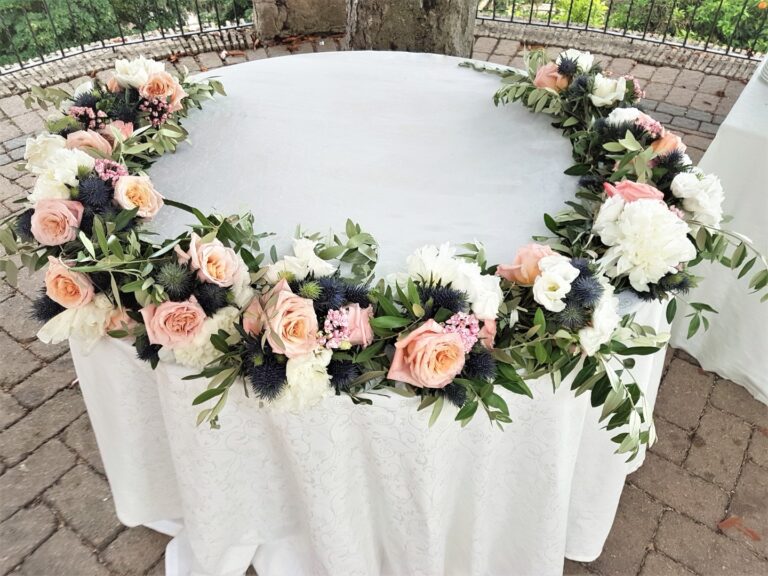 Garland of peach roses and thistle circling a white round table outdoors, Fiori Amore Fantasia