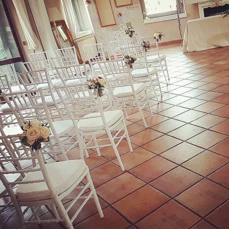 White chairs for a ceremony, each marked with a small floral posy, Fiori Amore Fantasia