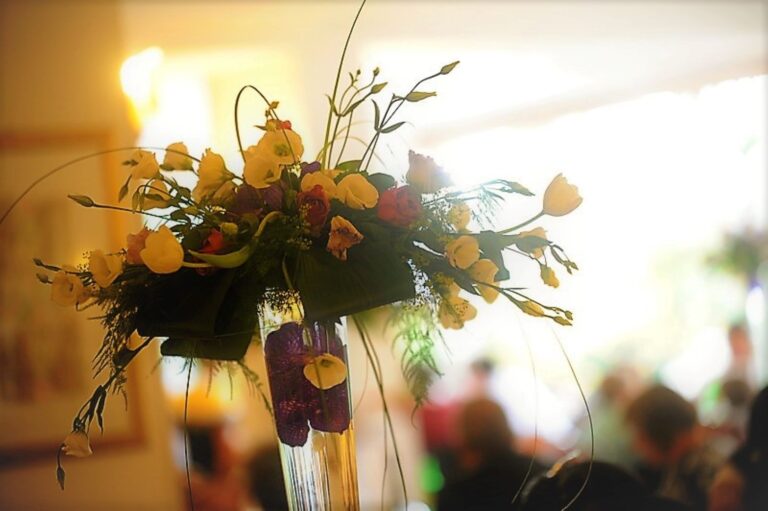 Tall yellow and orange arrangement glowing under reception lighting, Fiori Amore Fantasia