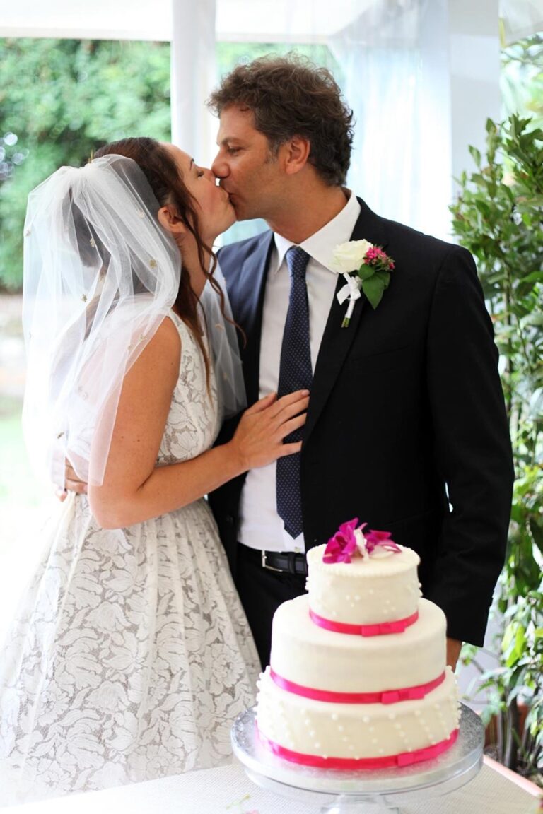 Newlyweds kissing beside their wedding cake, Fiori Amore Fantasia