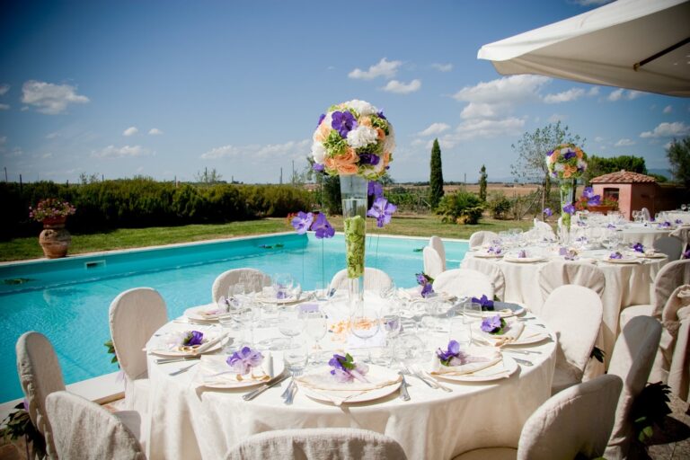 Round reception table with a tall floral centrepiece beside a pool, set in open countryside, Fiori Amore Fantasia