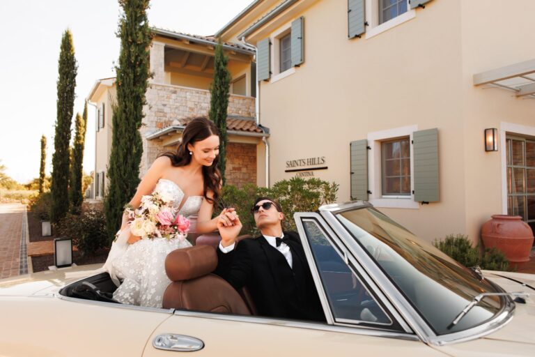 A bride and groom in a cream convertible in front of Saints Hills, Flammeum