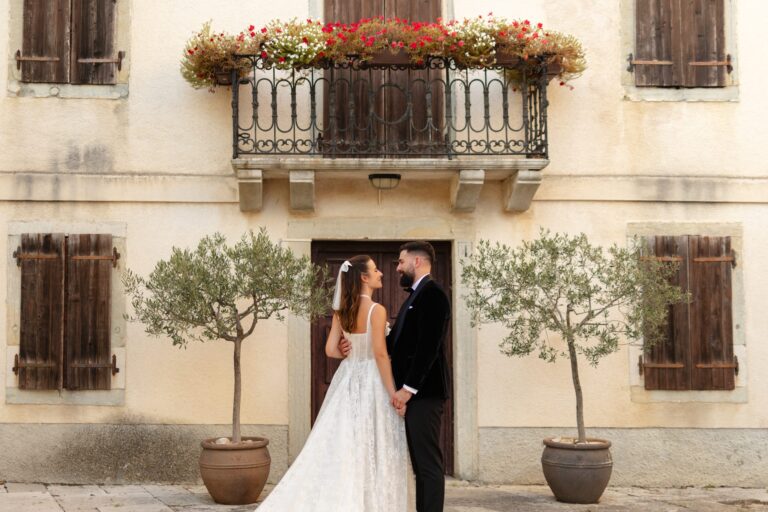 A bride and groom in a villa doorway framed by olive trees and a flowered balcony, Istria, Flammeum