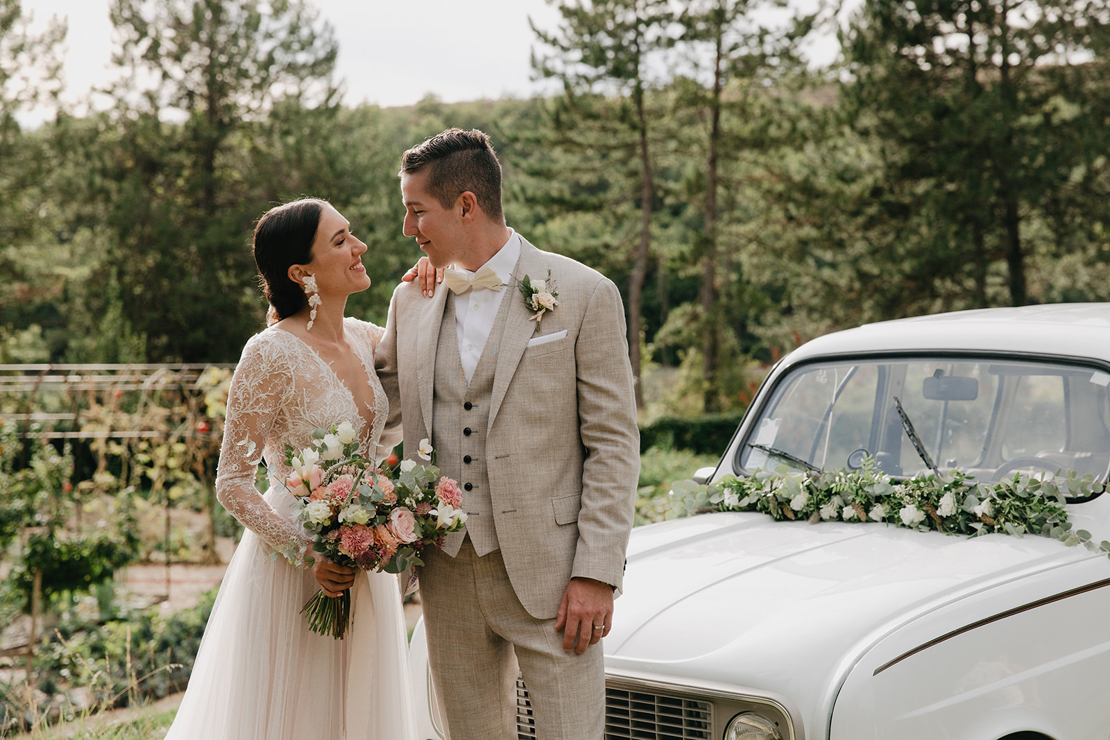 A couple beside a white vintage car decorated with a floral garland, Fleurs design By Faustine