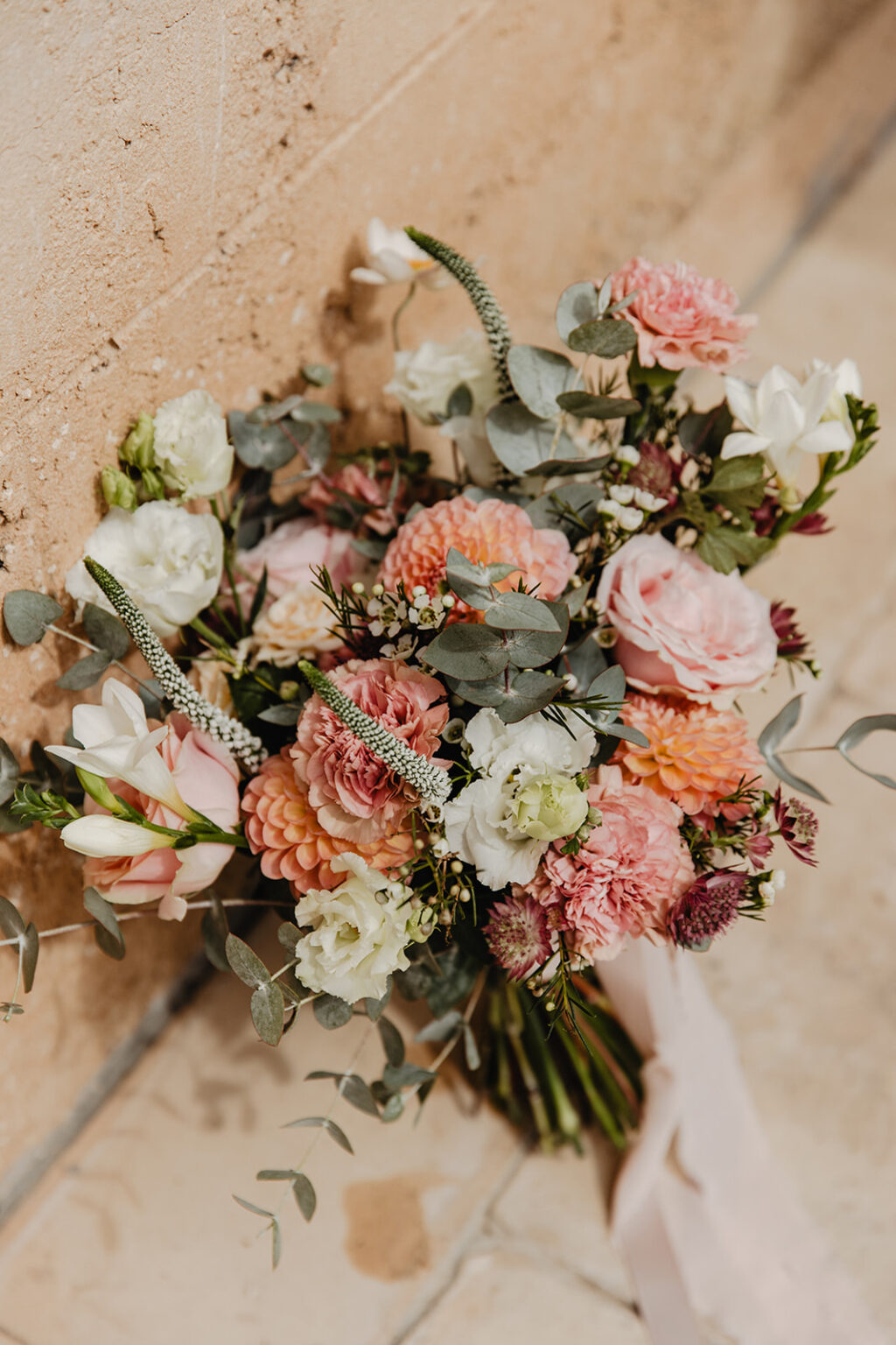 A hand-tied bridal bouquet of peach roses, pink blooms, white lisianthus and eucalyptus
