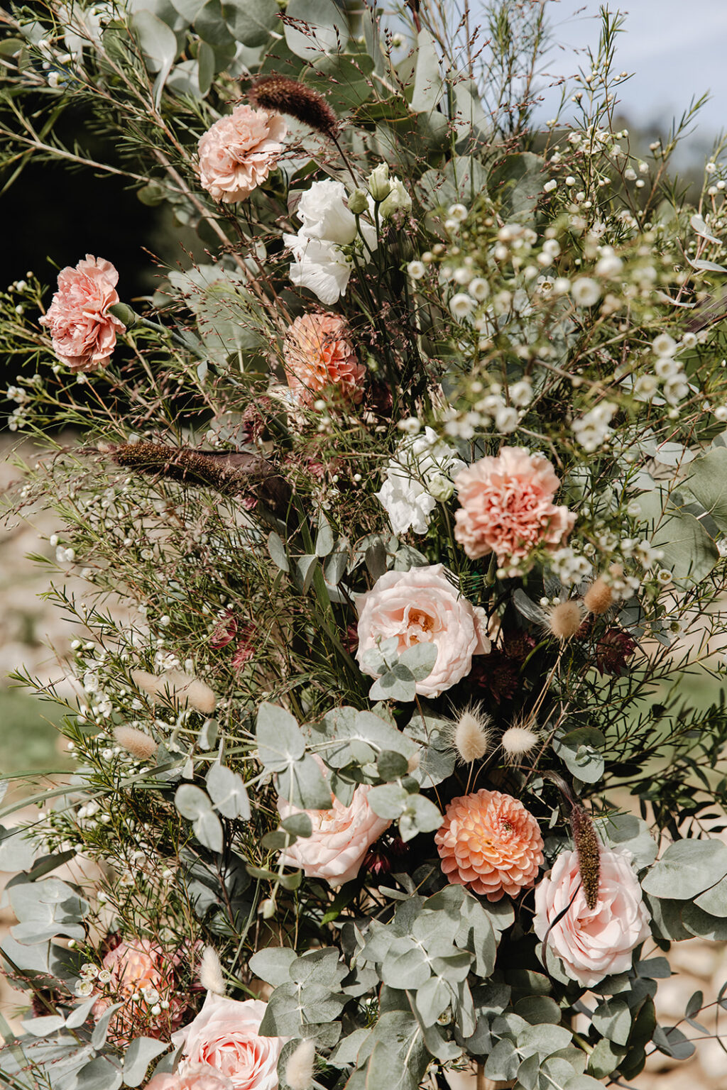 A tall natural floral installation of peach roses, carnations, dahlias and eucalyptus