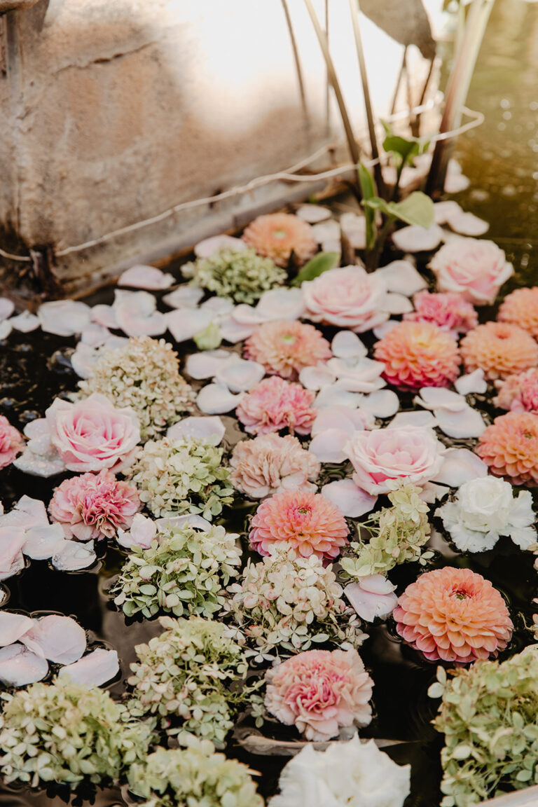 Dahlias, hydrangeas and roses floating in a stone fountain basin, Fleurs design By Faustine
