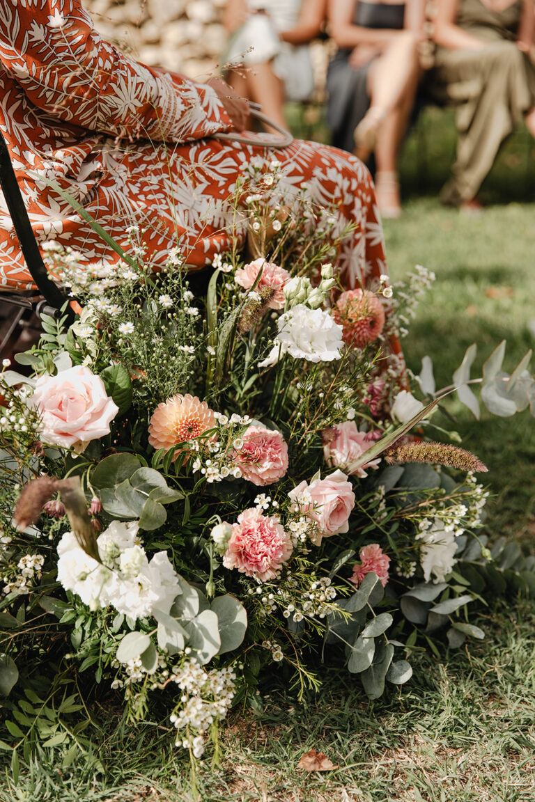 A low aisle arrangement of roses, carnations and eucalyptus beside seated ceremony guests, Fleurs design By Faustine