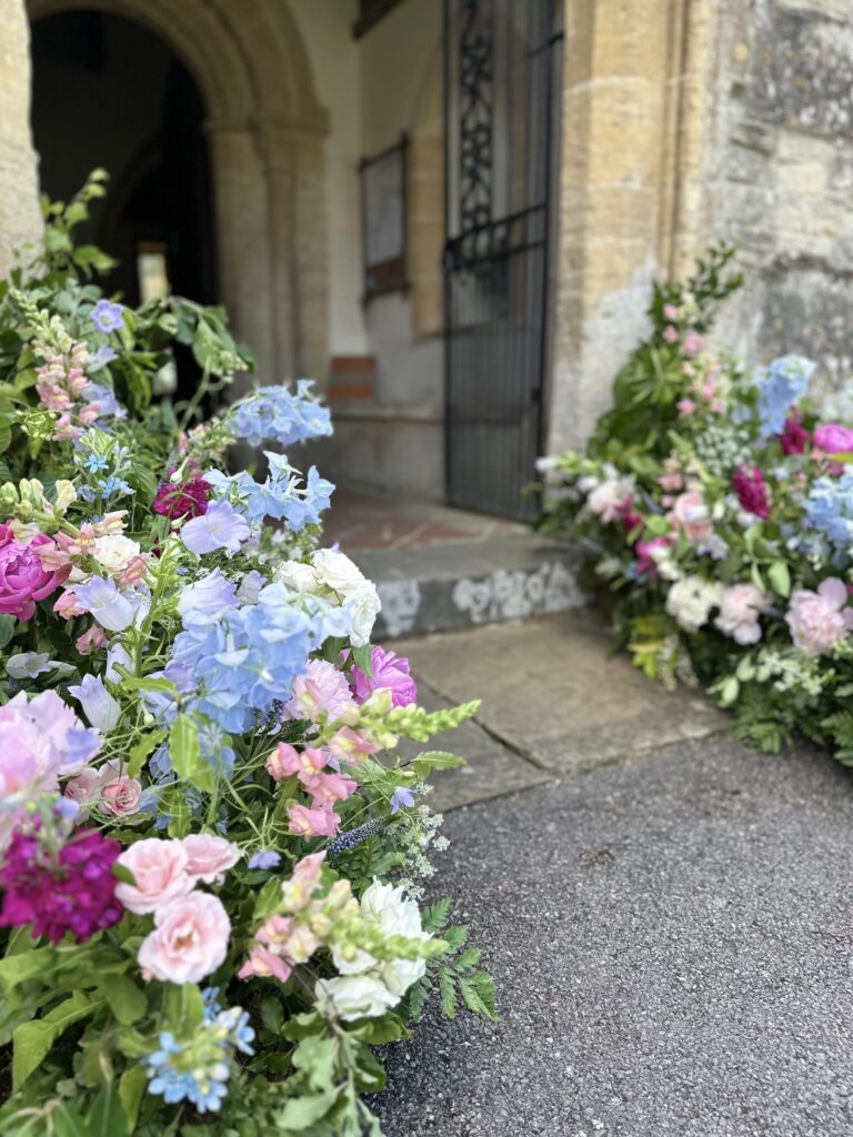 Delphinium, campanula and rose flank a church entrance, Foxgloves and Roses