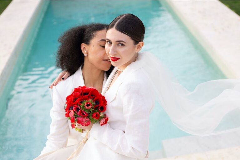 Two brides in a pool with a bouquet of red roses, a same-sex wedding at Riva Lofts, Florence, Franci's Flowers Wedding Design