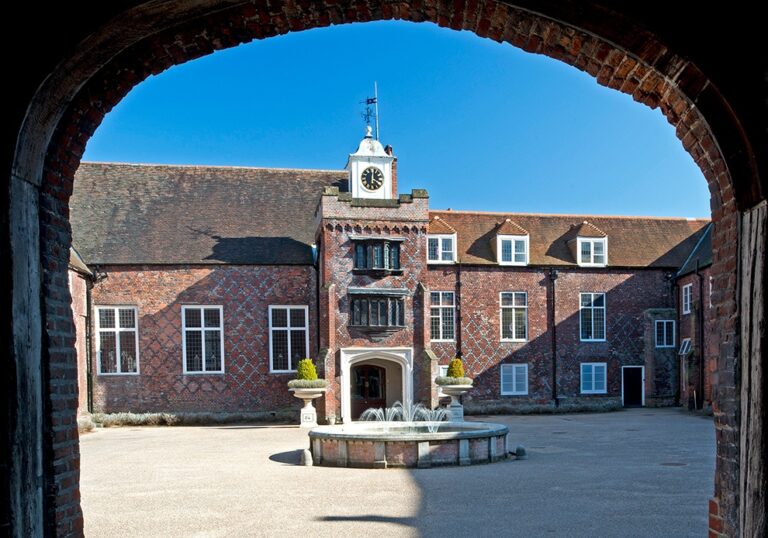 The Tudor Courtyard and clock tower on a bright day, glimpsed through an arch, Fulham Palace