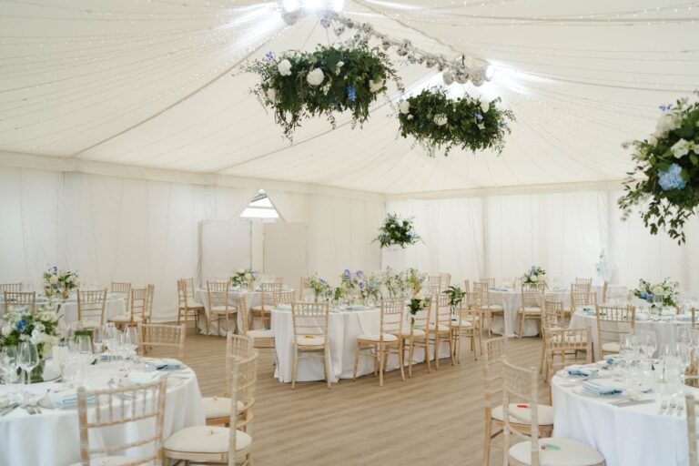The Chaplain's Marquee dressed for a wedding breakfast, round tables beneath a suspended floral chandelier, Fulham Palace