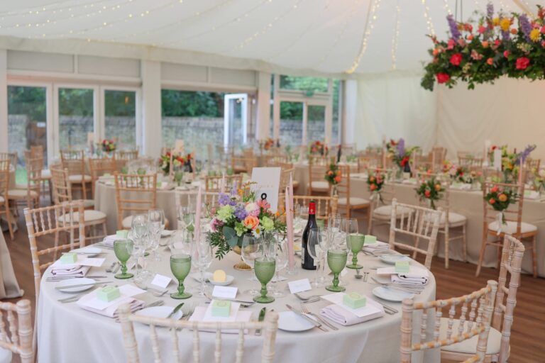 Round tables in the Chaplain's Marquee set with green glassware and low arrangements, Fulham Palace