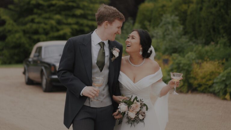 Amy and Wesley laughing with drinks beside a vintage car at Avington Park, Gaetano Di Giacomo Media Production