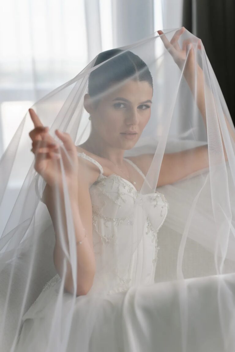 Bride lifting her veil in soft window light, Geta Ungurean Agency
