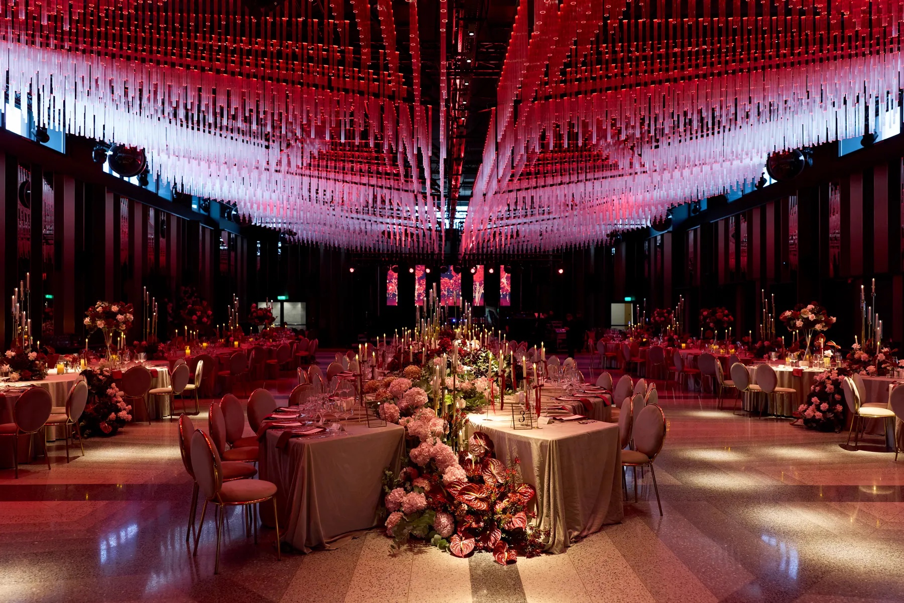 Reception hall with a suspended red and pink ceiling installation and long floral tables, Geta Ungurean Agency